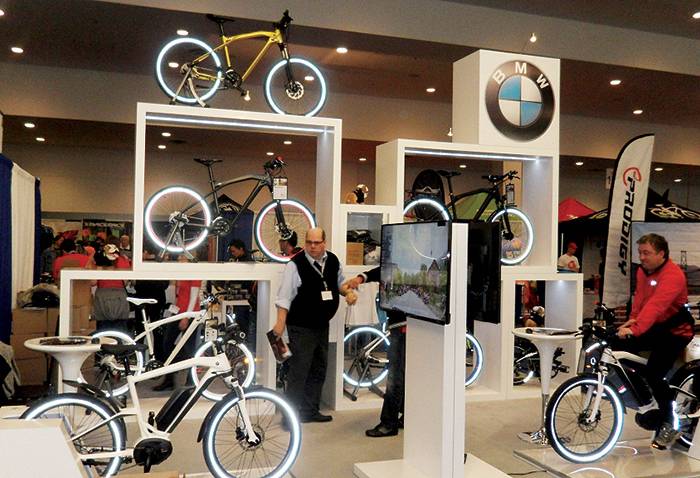 A BMW-branded exhibit showcasing bicycles, including electric models, displayed on stands with glowing rims, attended by staff and visitors.