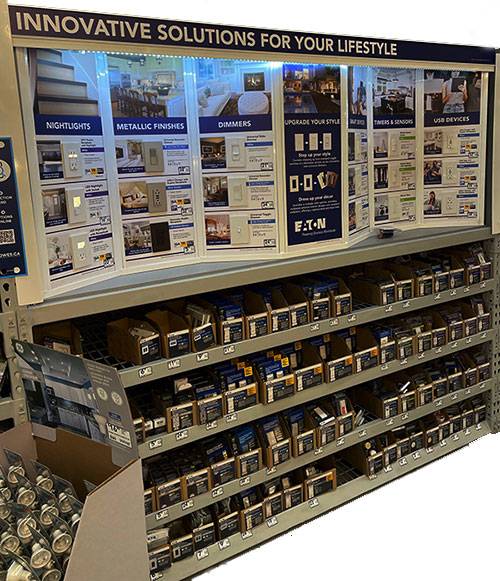 A merchandise display for Eaton electrical products featuring innovative solutions such as nightlights, metallic finishes, dimmers, USB devices, timers, and sensors, arranged neatly on shelves.